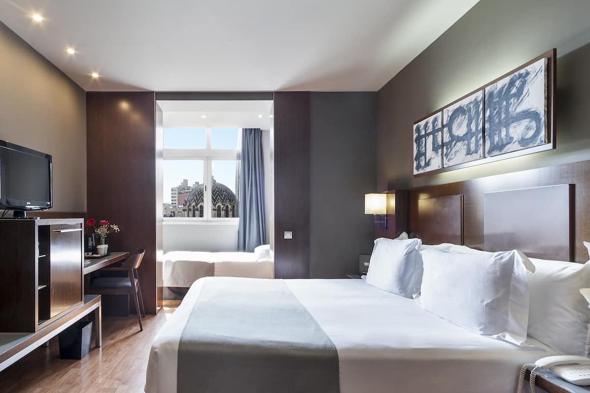 Habitación de hotel con una cama grande, un escritorio, un televisor y una ventana con cortinas.