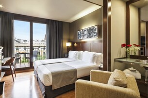 A hotel room with a large bed, a desk, a chair, a mirror, and a view of the city.
