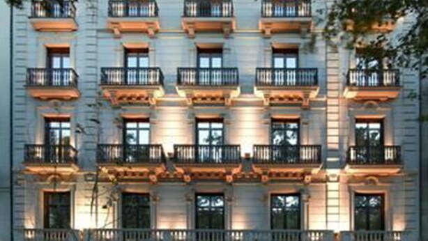 Un hôtel à plusieurs étages doté de balcons, d’un magasin au rez-de-chaussée et d’un panneau indiquant un parking.