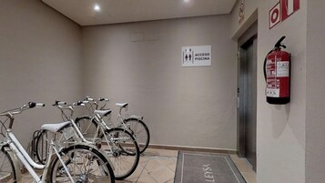 A hallway with bicycles parked against the wall, a fire extinguisher mounted on the wall, and a sign indicating access to the pool.