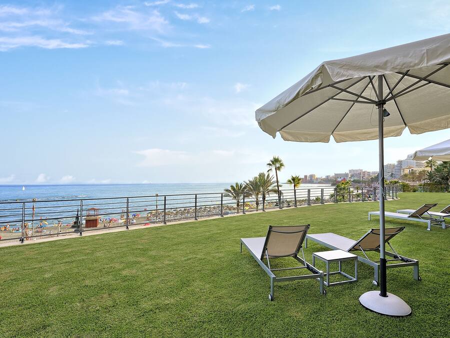 Terrassa amb gespa, seients de sofà i un parasol amb vista a la platja.