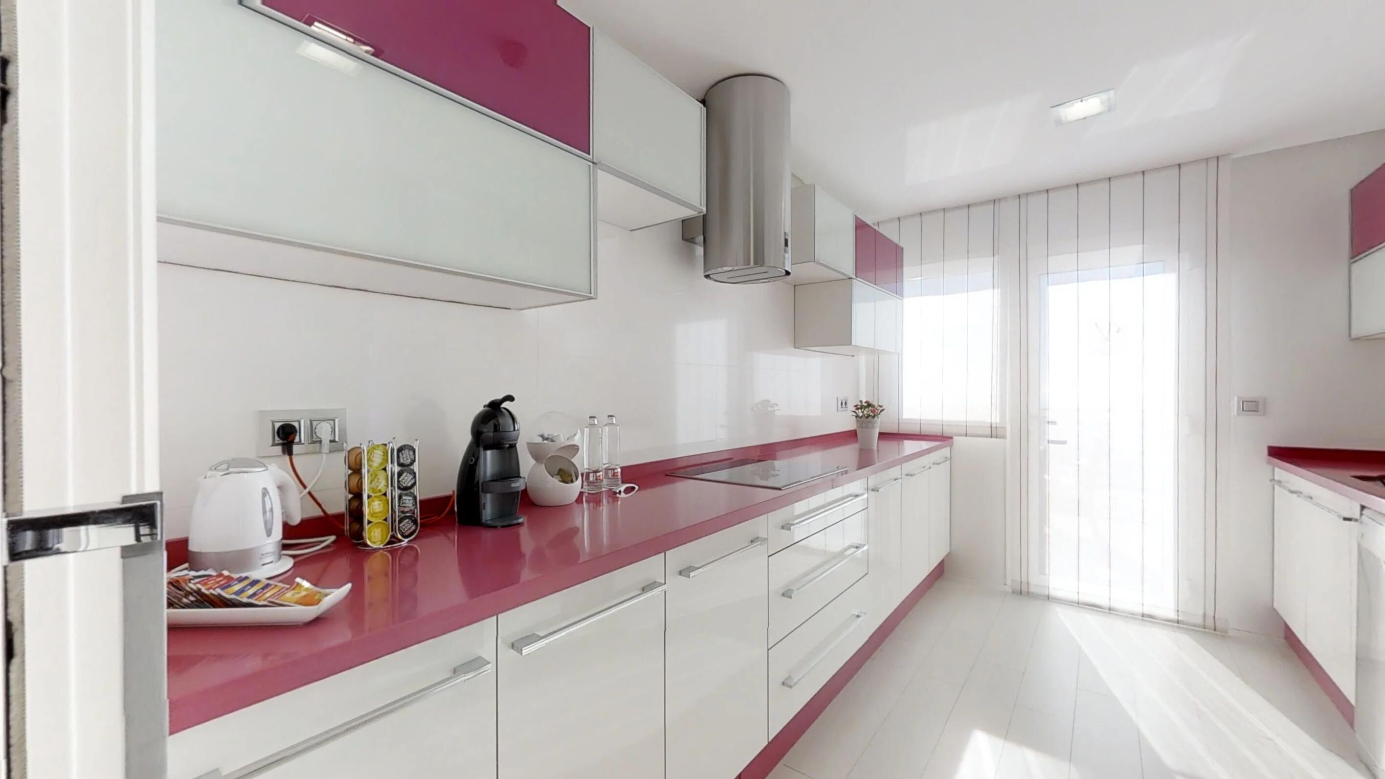 Una cocina moderna con armarios blancos, encimera roja y estufa integrada.