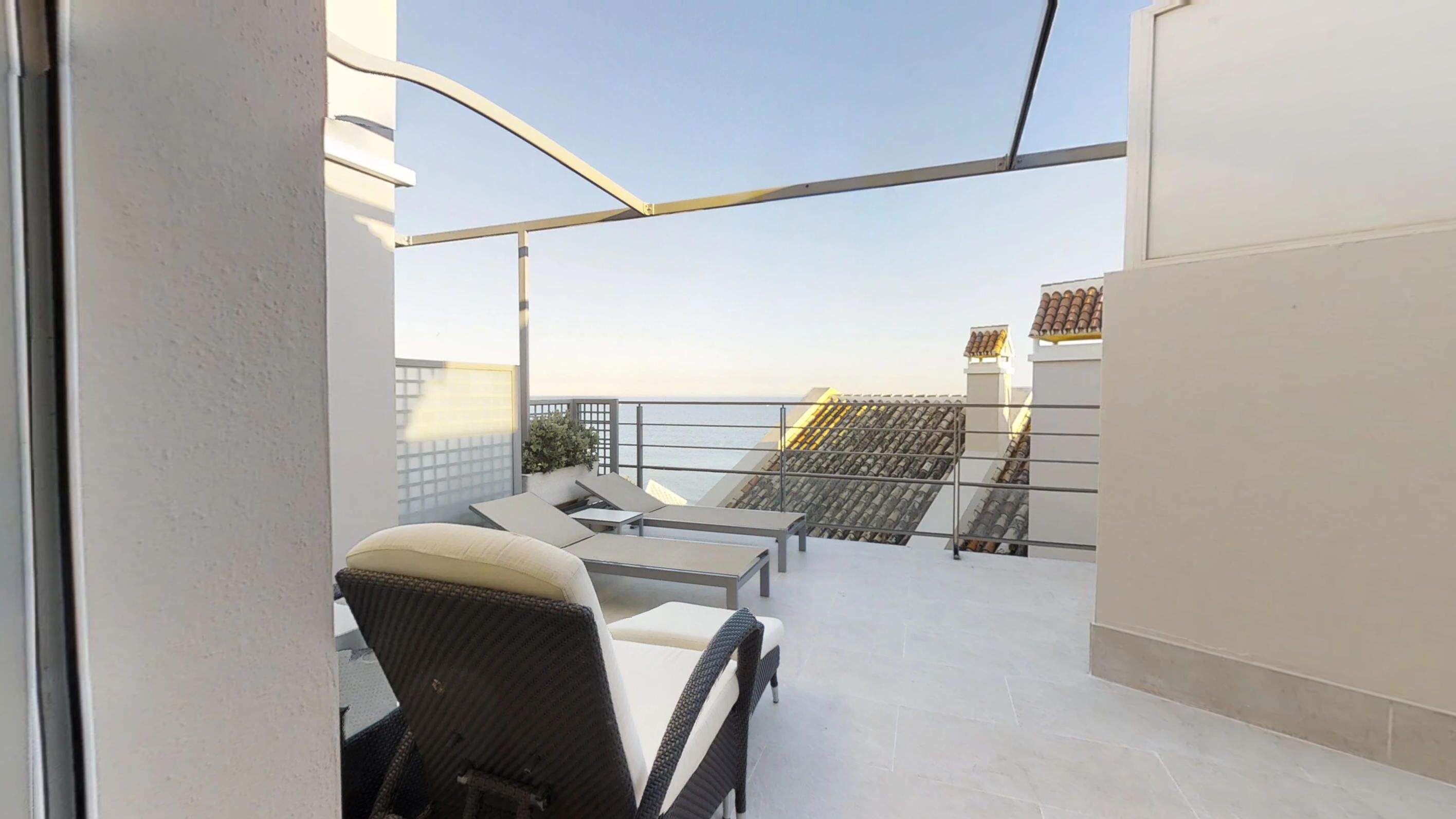 A balcony with a view of the sea, featuring a seating area with chairs and a table.