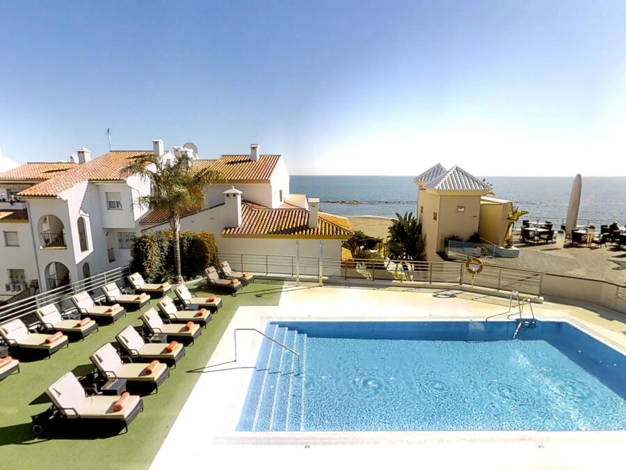A rooftop pool with lounge chairs, a clear view of the sea, and a building with a tiled roof.