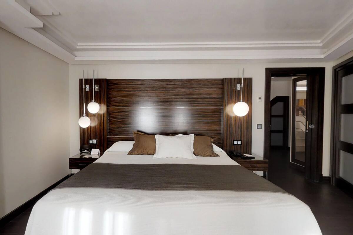 Ein modernes Hotelzimmer mit einem großen Bett, einem Holz-Kopfteil und zwei Nachttischen mit Lampen.