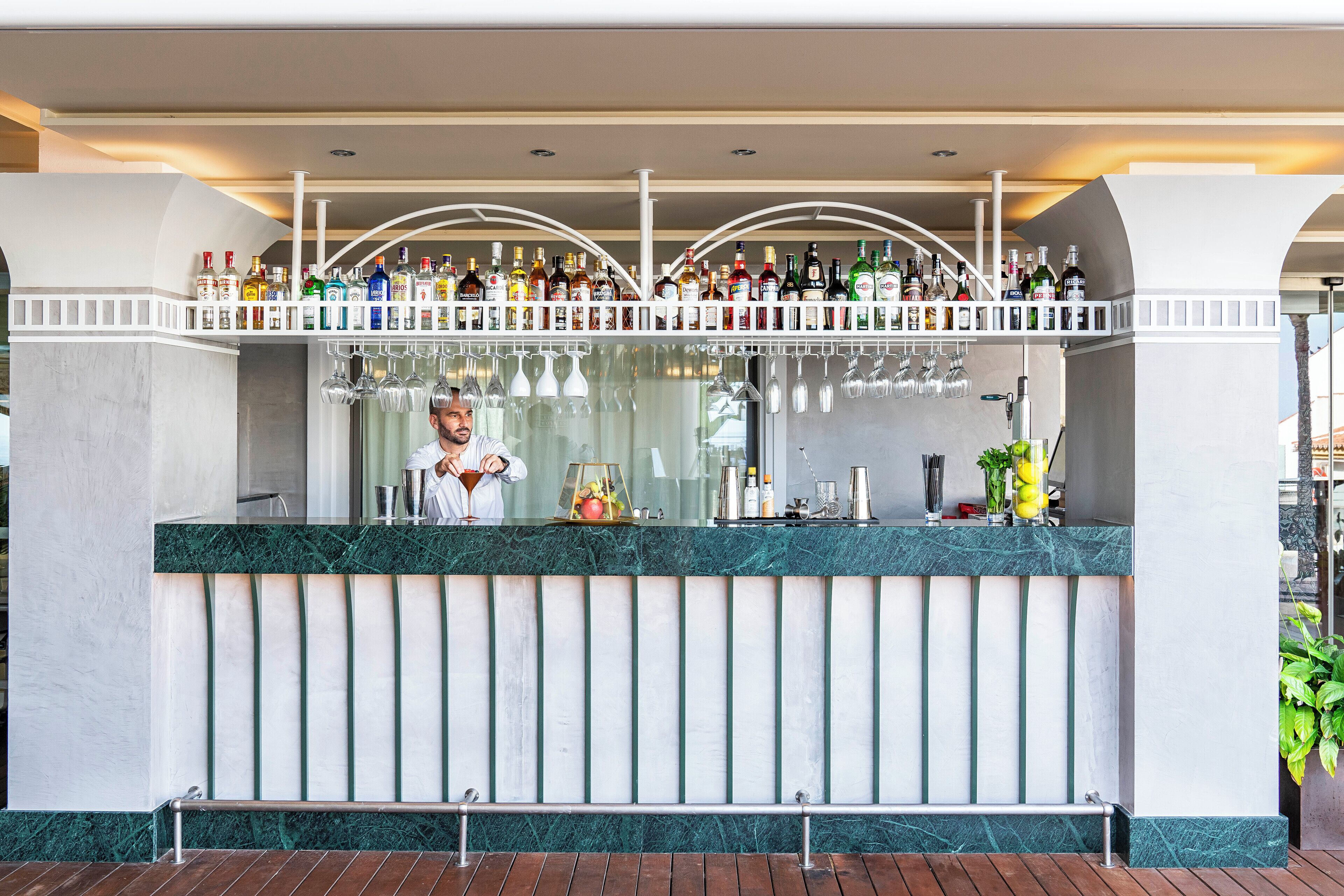 A bar area with a bartender, a variety of liquor bottles, and a marble counter.