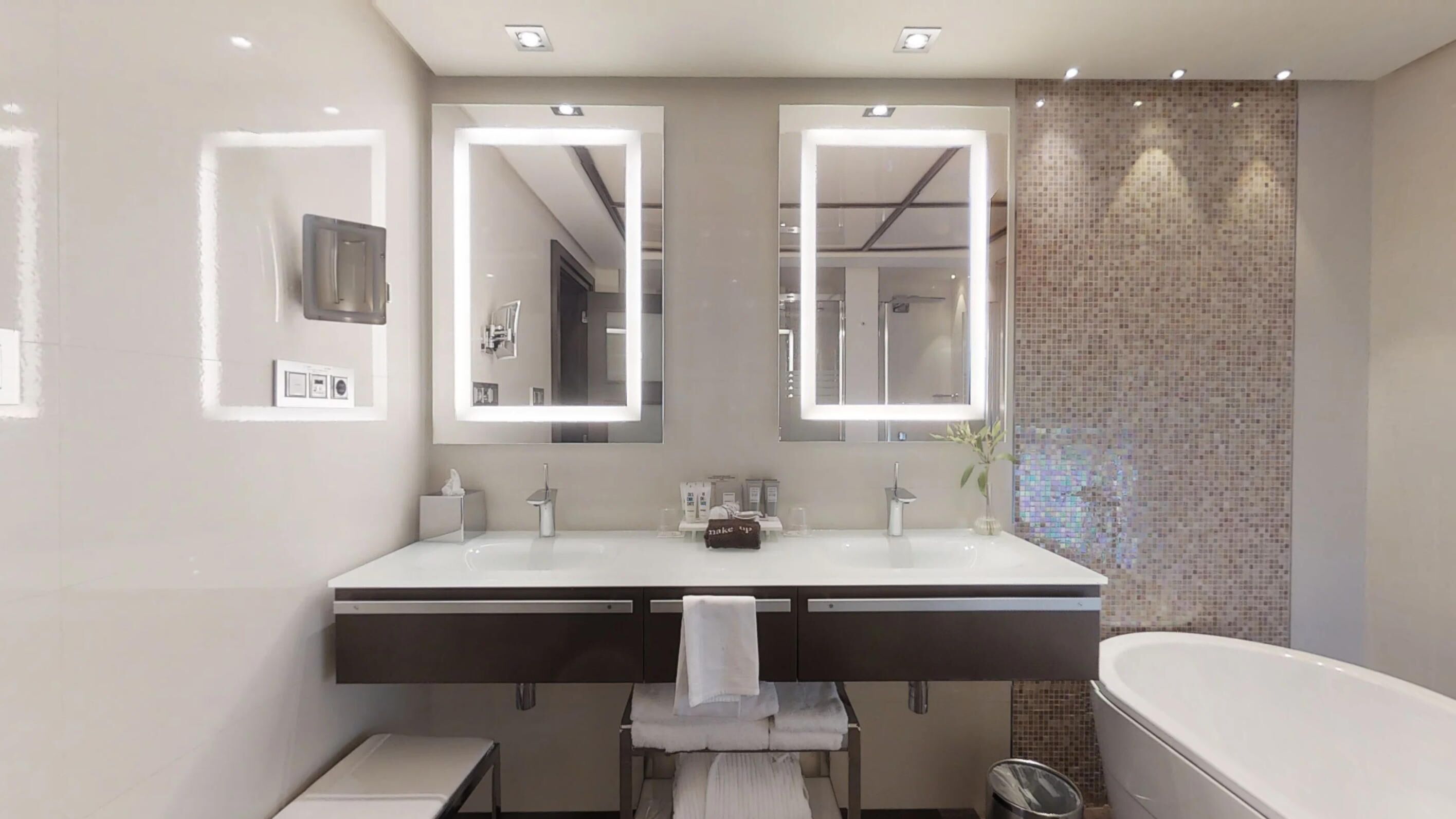 A modern bathroom with two sinks, a large mirror, a bathtub, and a tiled wall.