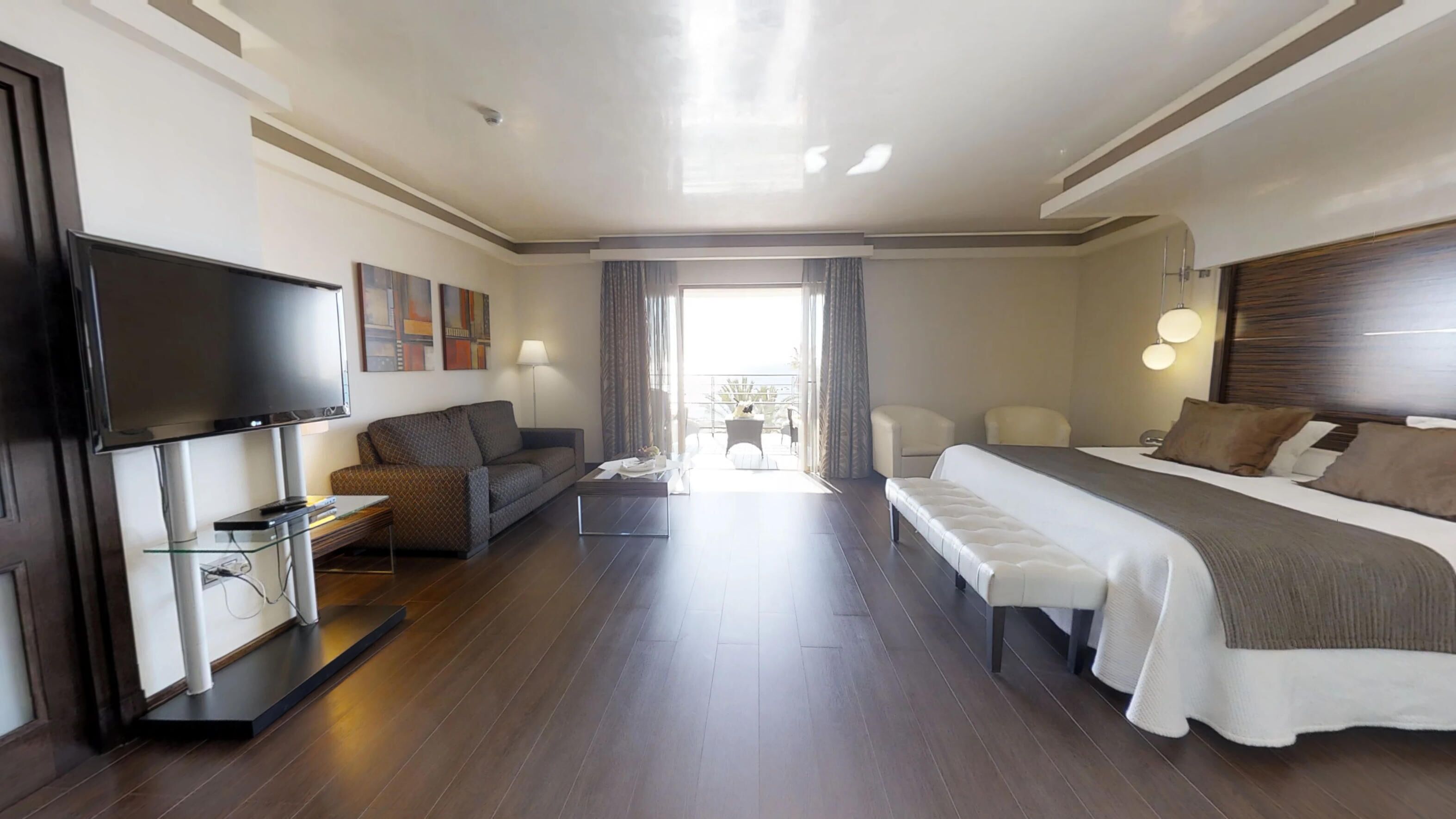 Een moderne hotelkamer met een groot bed, een bank, een televisie en een balkon met gordijnen.
