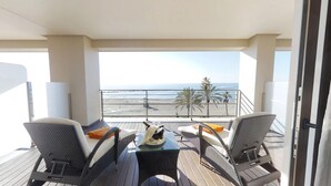 A balcony with wicker furniture, a glass table, and a view of the beach and ocean.