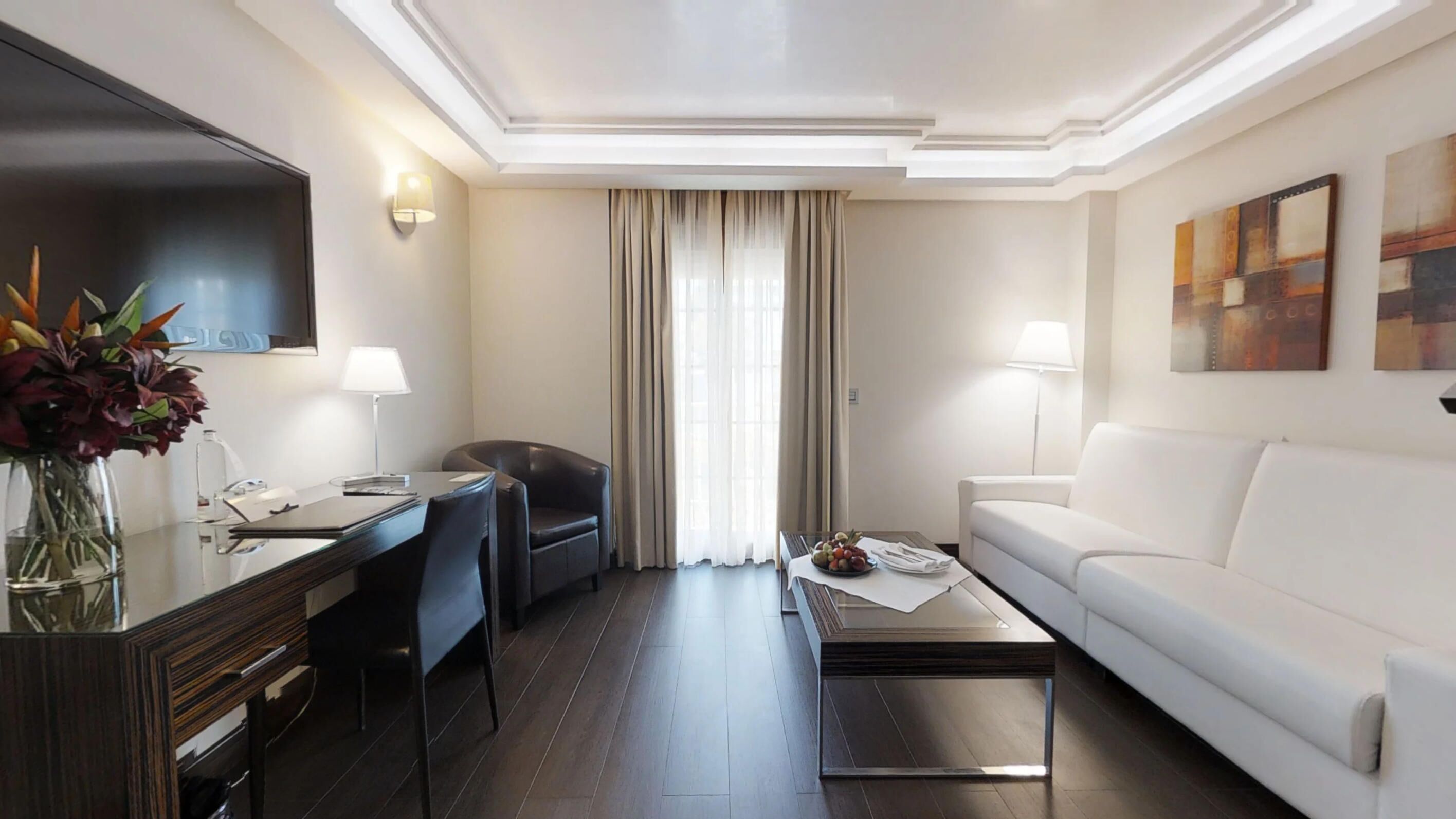 Una habitación de hotel moderna con escritorio, silla, sofá blanco y una mesita de café.