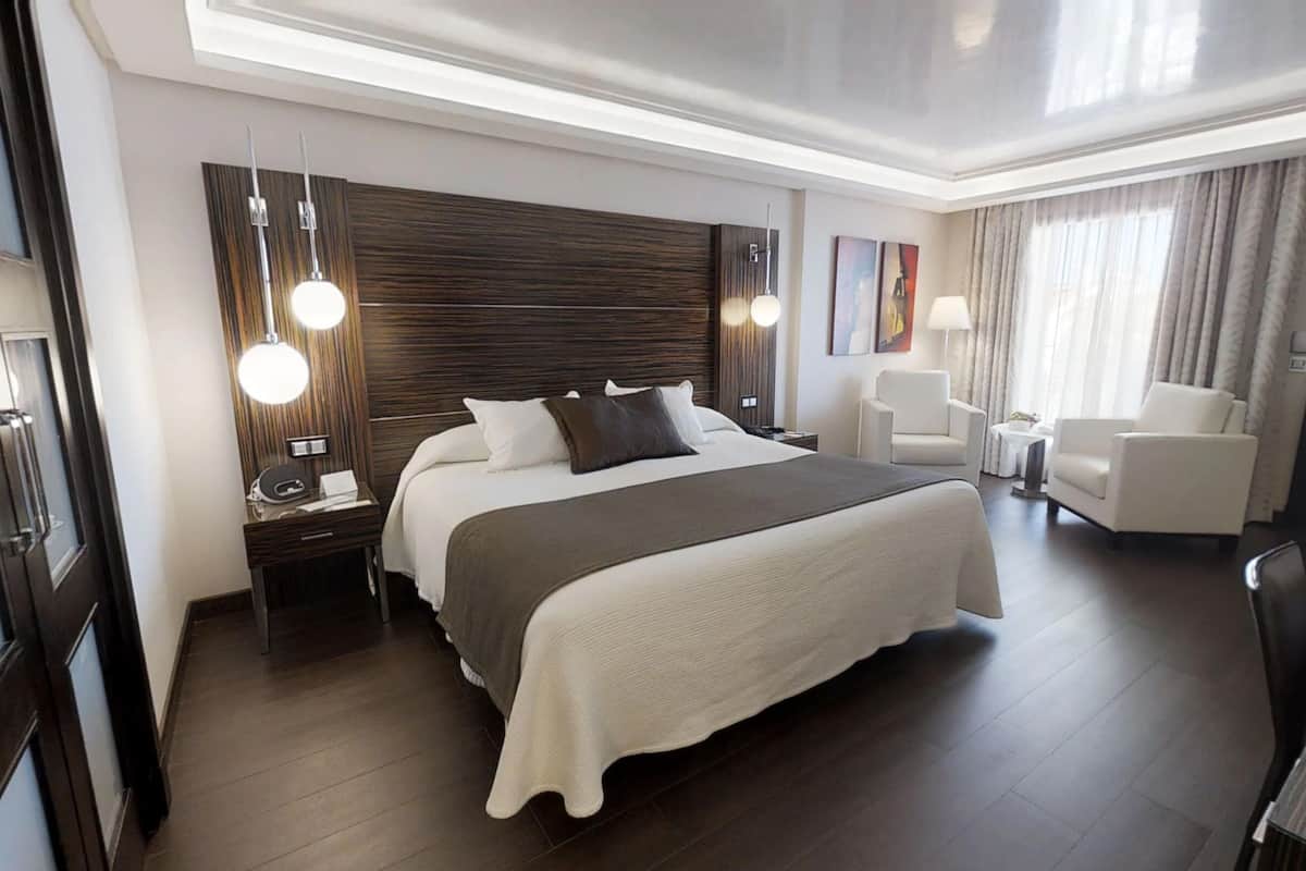 A modern hotel room with a large bed, bedside tables, a desk, and a chair.