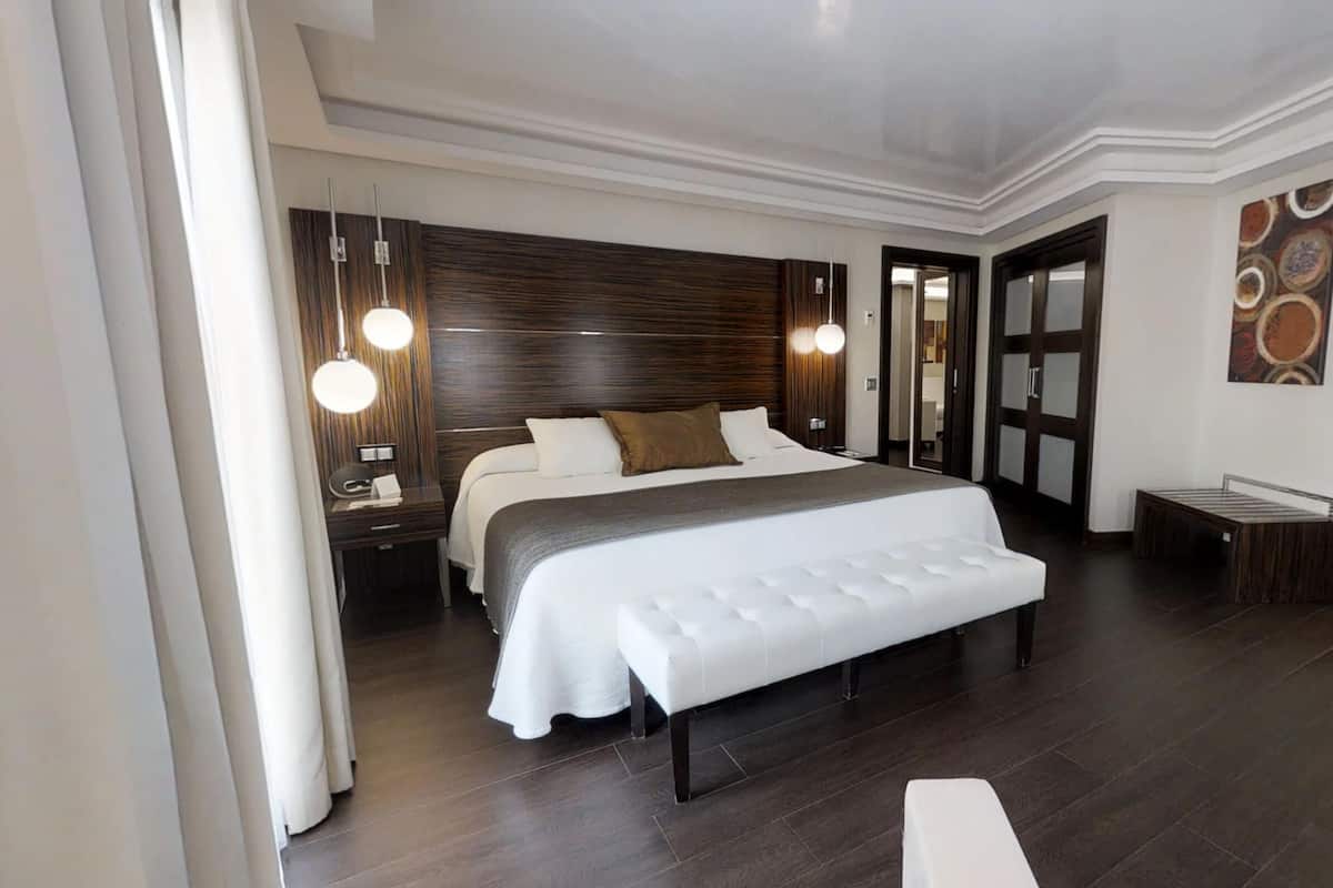 Ein modernes Hotelzimmer mit einem großen Bett, Nachttischen, einer Bank und einer Tür zu einem Badezimmer.