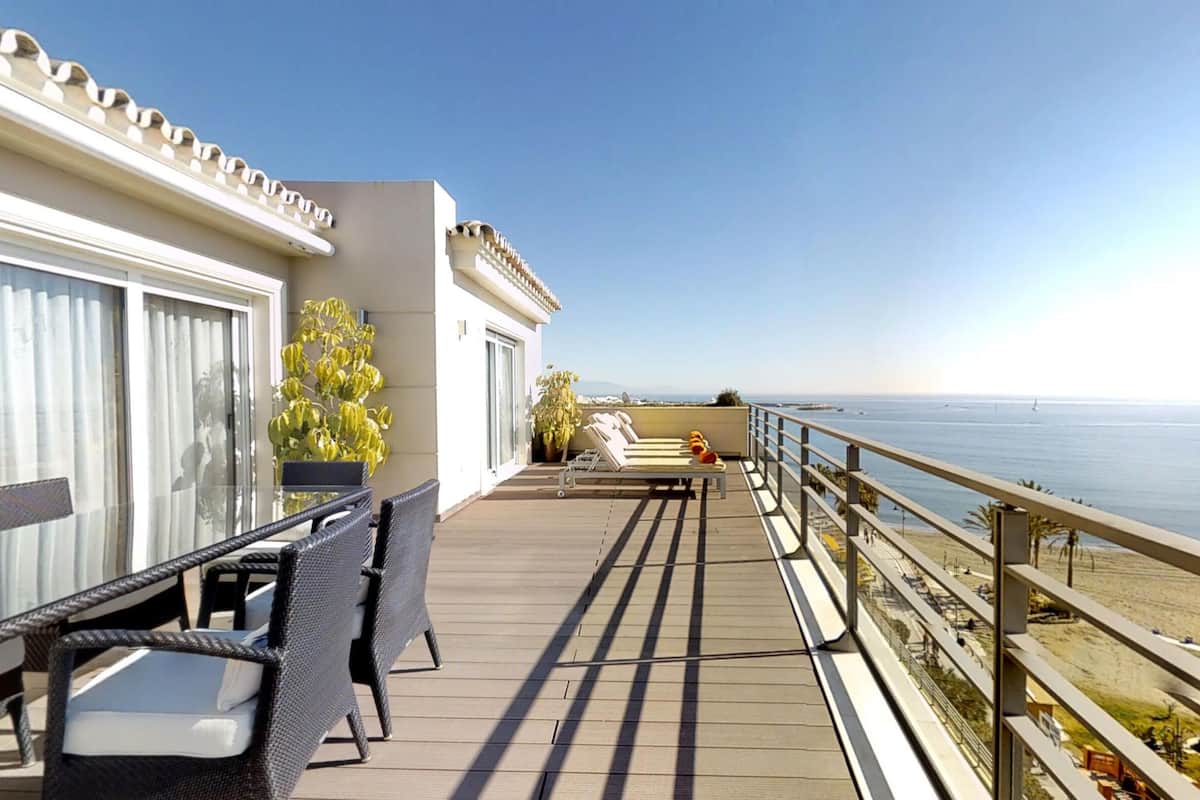 Ein Balkon mit Tisch und Stühlen, einer Liege und Blick aufs Meer.