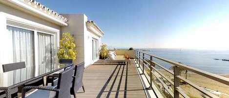 A balcony with a table and chairs, a lounge chair, and a view of the sea.