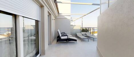 A modern balcony with a glass door, two lounge chairs, a small table, and a potted plant.