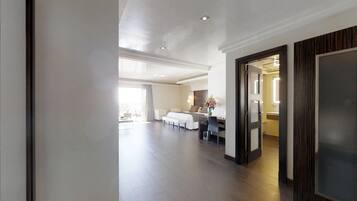 A spacious hotel room with a large bed, a sitting area with a table and chairs, a desk, and a view of the outdoors.