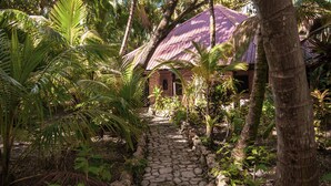 Un sendero de piedra que lleva a una construcción rústica con techo de paja, rodeada de exuberante vegetación tropical.