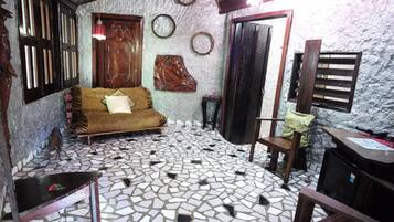 Una habitación con piso de mosaico, un sofá con cojines, una puerta de madera y una pequeña mesa.