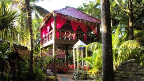 Un resort tropical con un pabellón de techo de paja, un sendero con mosaicos y abundante vegetación.