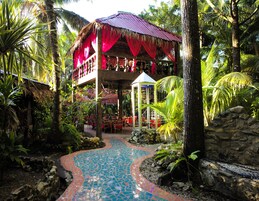 Un resort tropical con un pabellón de techo de paja, un sendero con mosaicos y abundante vegetación.