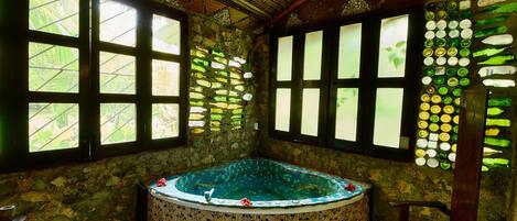 Habitación con bañera de mosaico, ventanas amplias con vistas y pared de piedra.