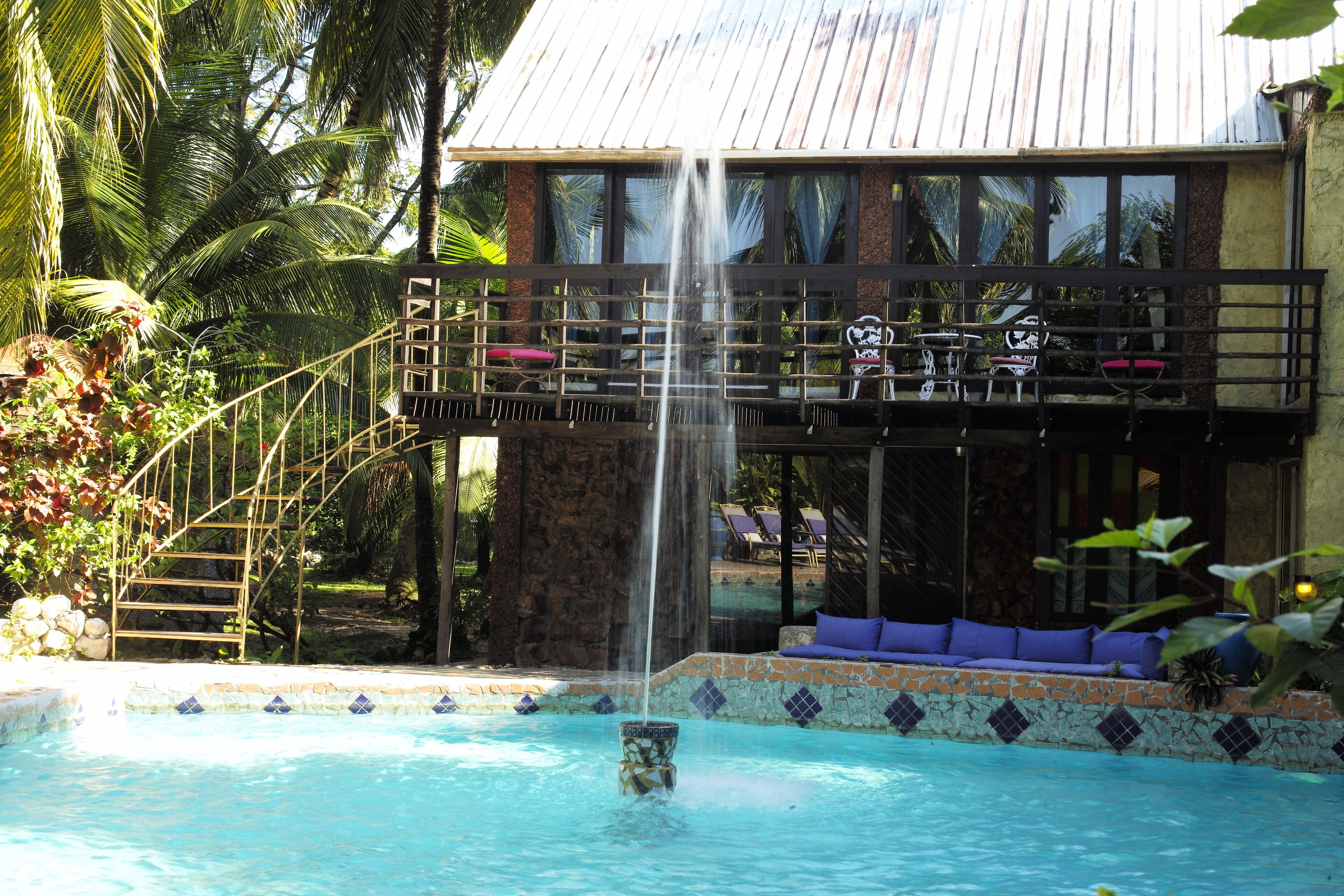 Une piscine agrémentée d’une cascade, une terrasse en bois avec des chaises longues et un bord de piscine revêtu de pierres.