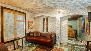 Una habitación acogedora con pared de piedra, un banco acolchado, piso de baldosas y una ventana con persianas.