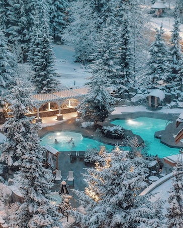 A snow-covered resort with a swimming pool, outdoor seating, and a gazebo.