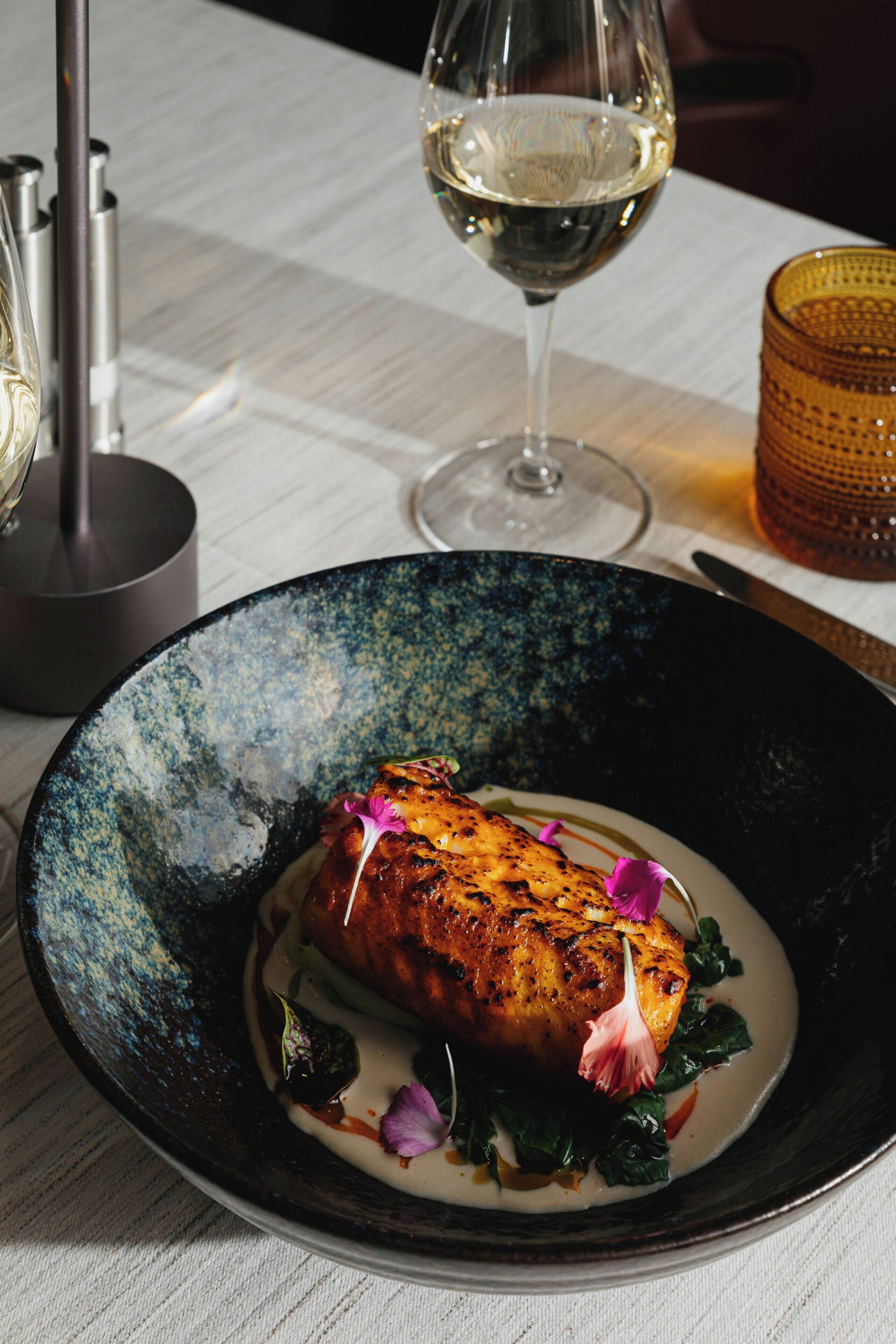 Un plato de comida con una copa de vino blanco y una vela sobre la mesa.