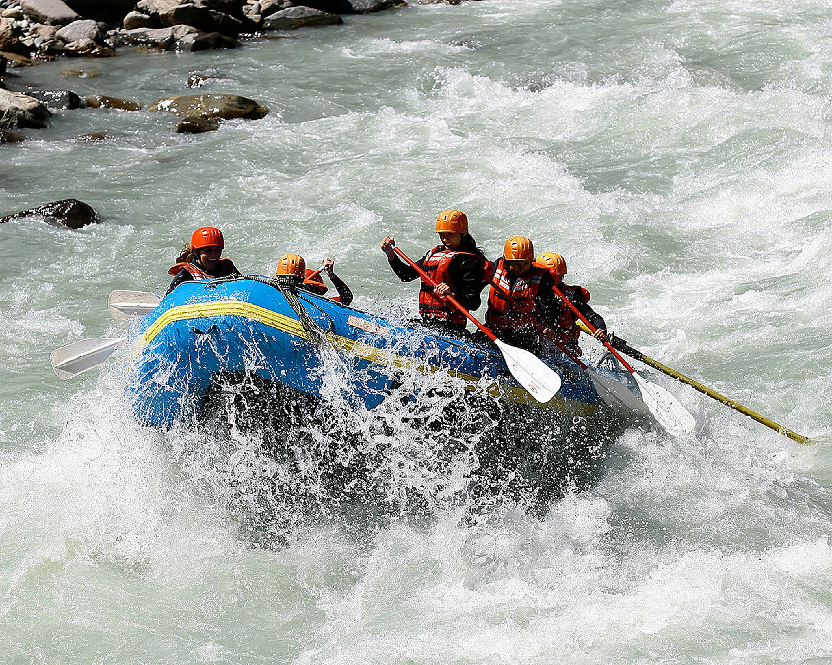 A group of people in a blue raft navigating through a river with rapids.