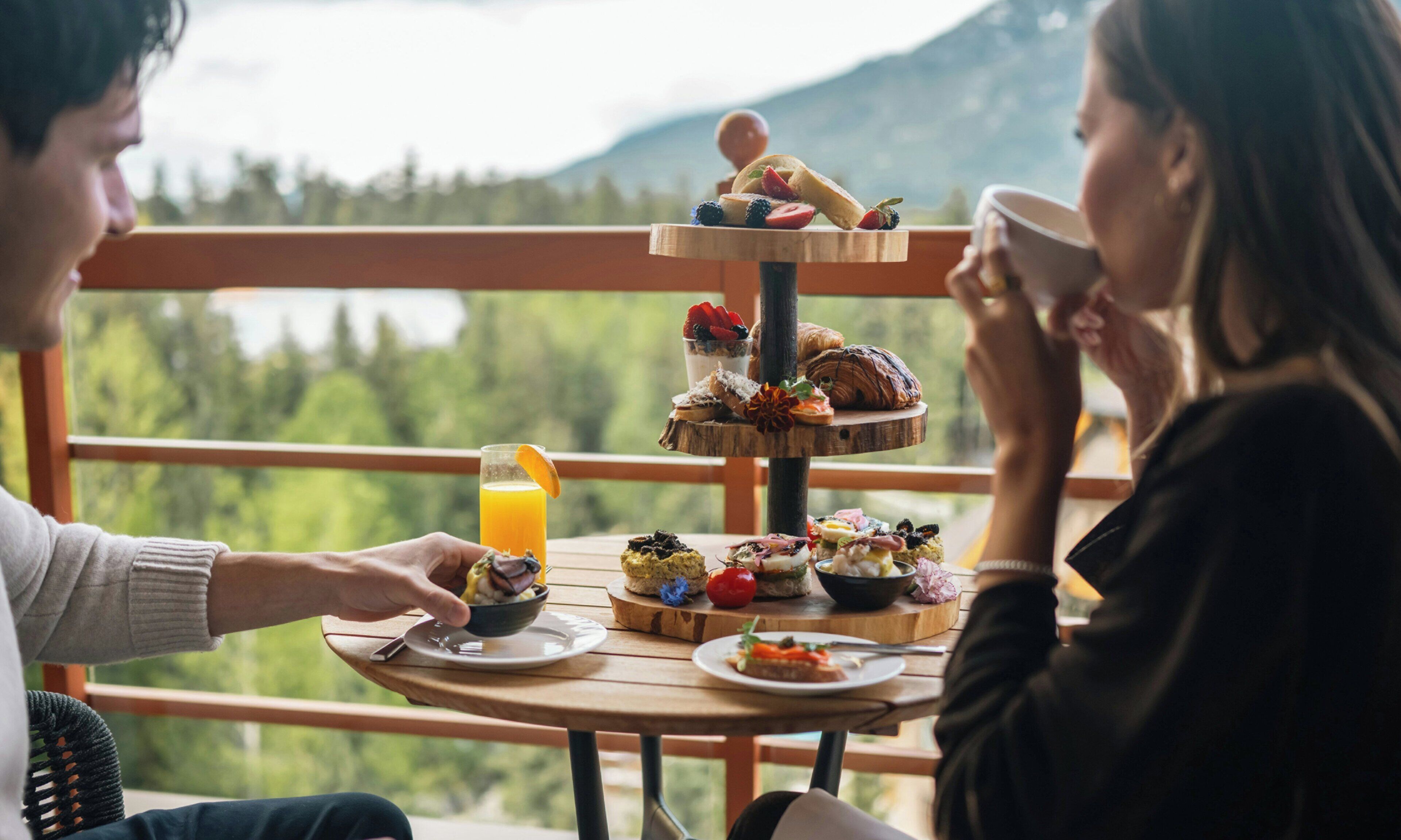 A wooden table with a tiered serving tray of food and a glass of orange juice.