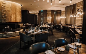 A restaurant with a central fire feature, multiple dining tables, and modern lighting fixtures. - Four Seasons Resort Whistler (Whistler)