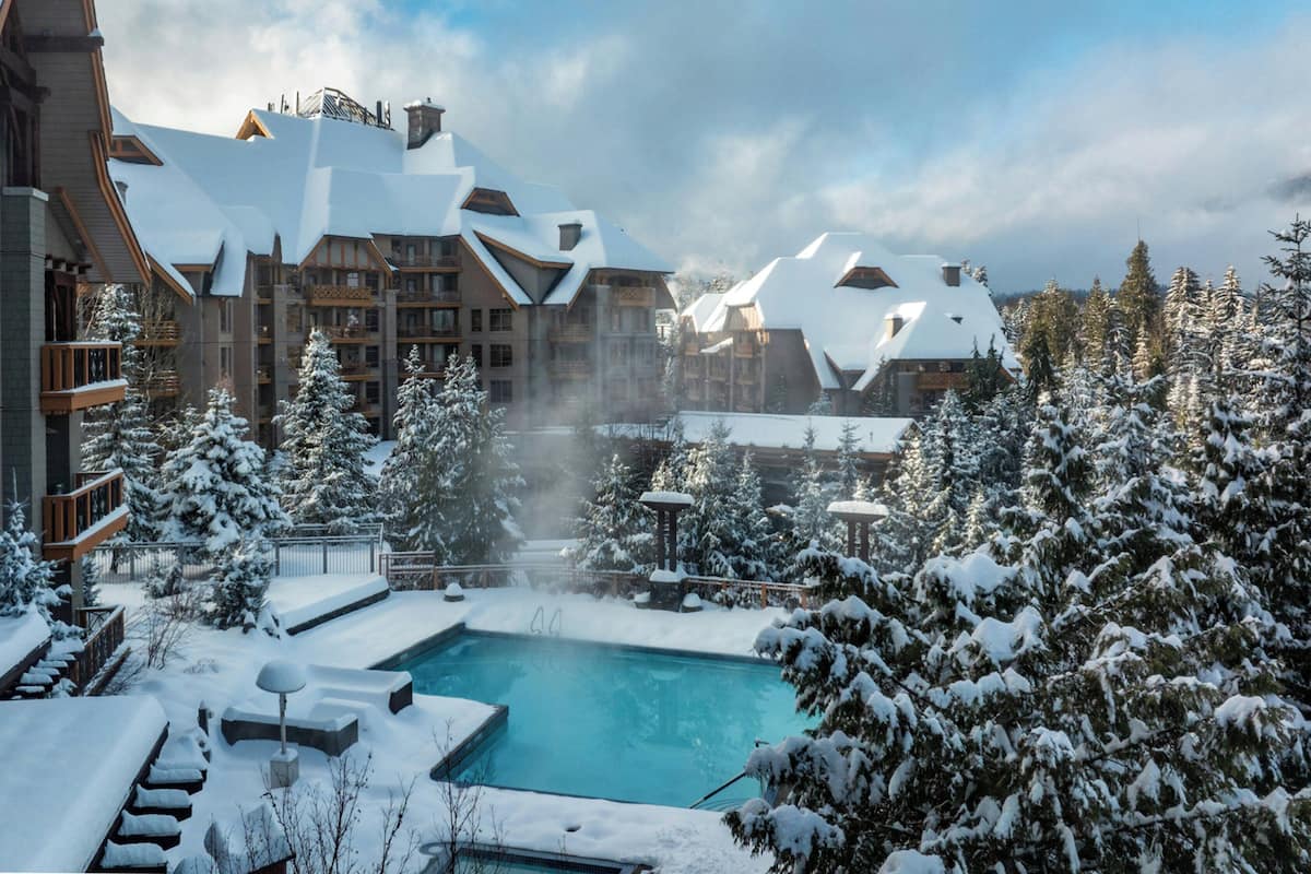 Un resort con piscina rodeado de árboles y edificios cubiertos de nieve.