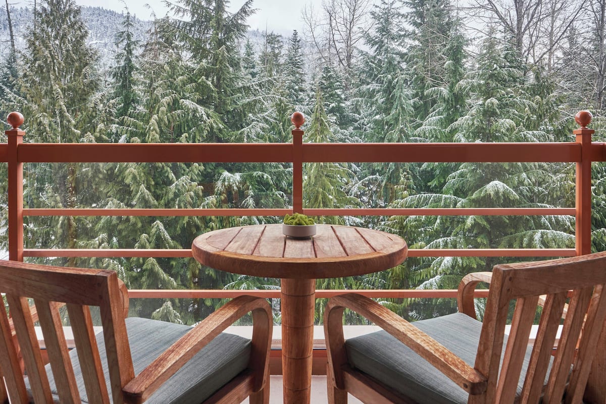 Un balcón de madera con una mesa redonda y dos sillas, con vistas a una zona boscosa.