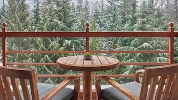 A wooden balcony with a round table and two chairs, overlooking a forested area.