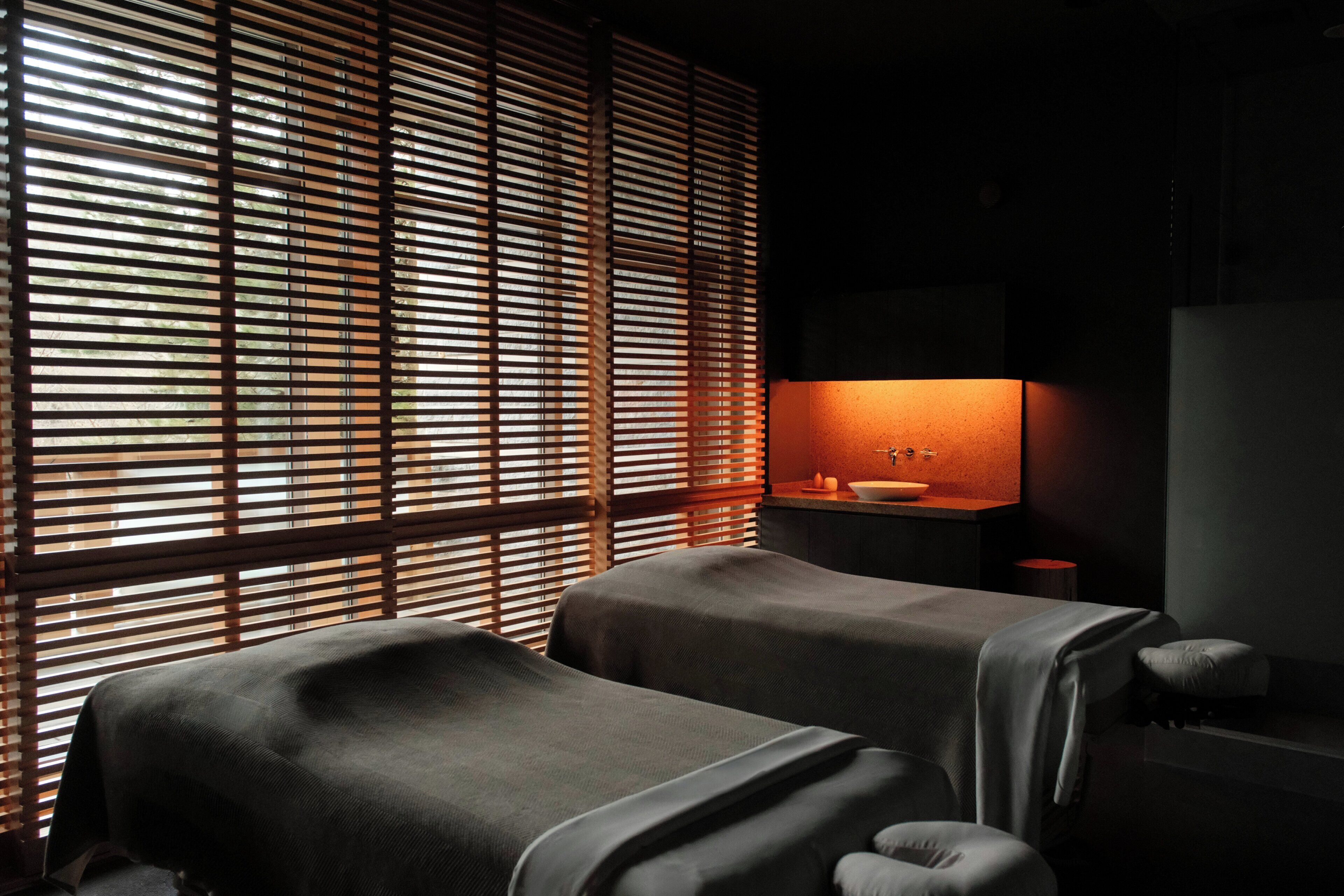 Un cuarto de spa con dos camillas de masaje, un lavamanos y una ventana con persianas.