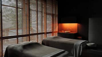 Un cuarto de spa con dos camillas de masaje, un lavamanos y una ventana con persianas.
