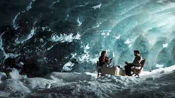 Interior de una cueva de hielo con dos personas sentadas en una mesa, rodeadas de nieve.