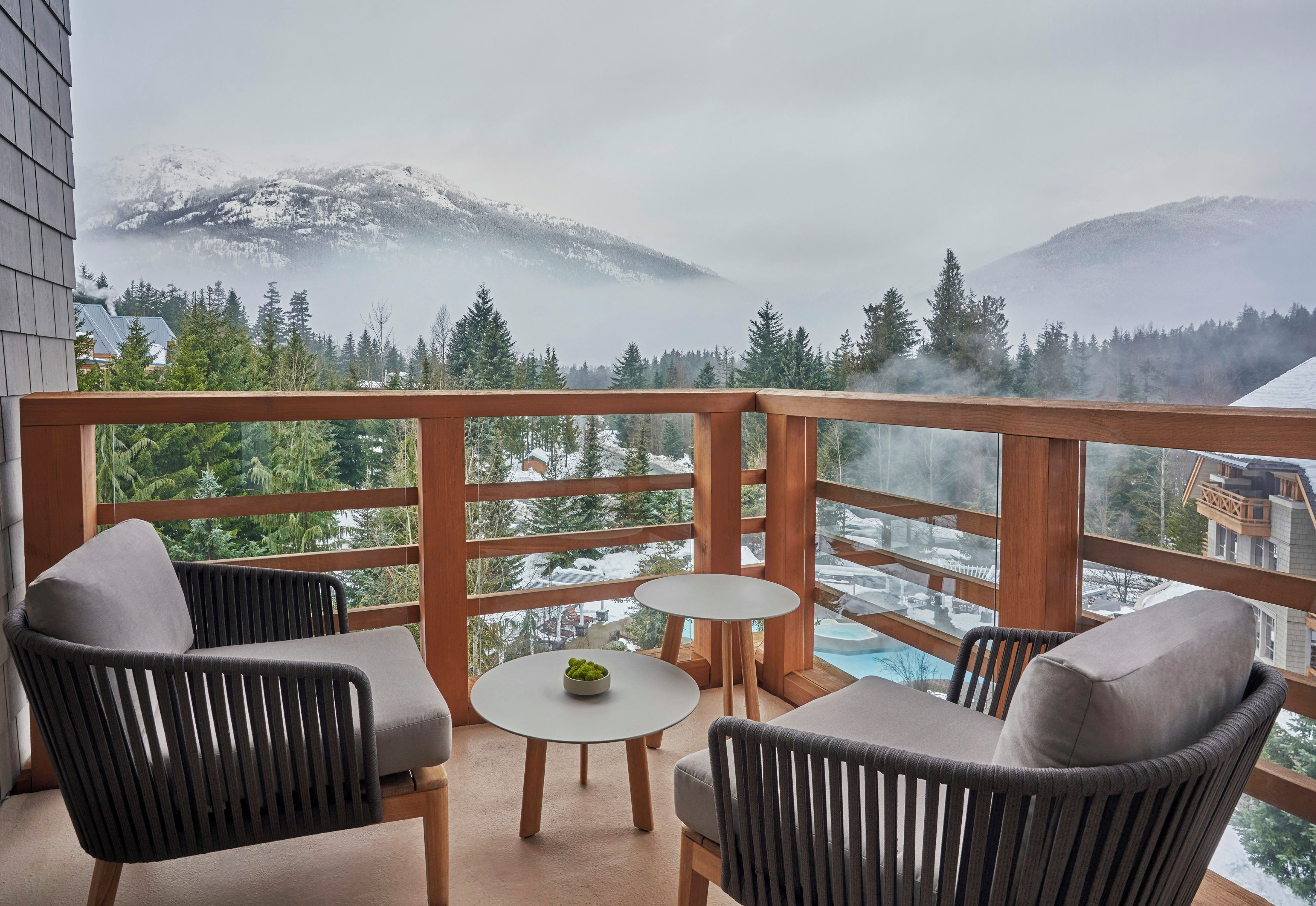 Un balcón con muebles de mimbre y una pequeña mesa, con vistas a un paisaje montañoso de picos nevados y árboles.