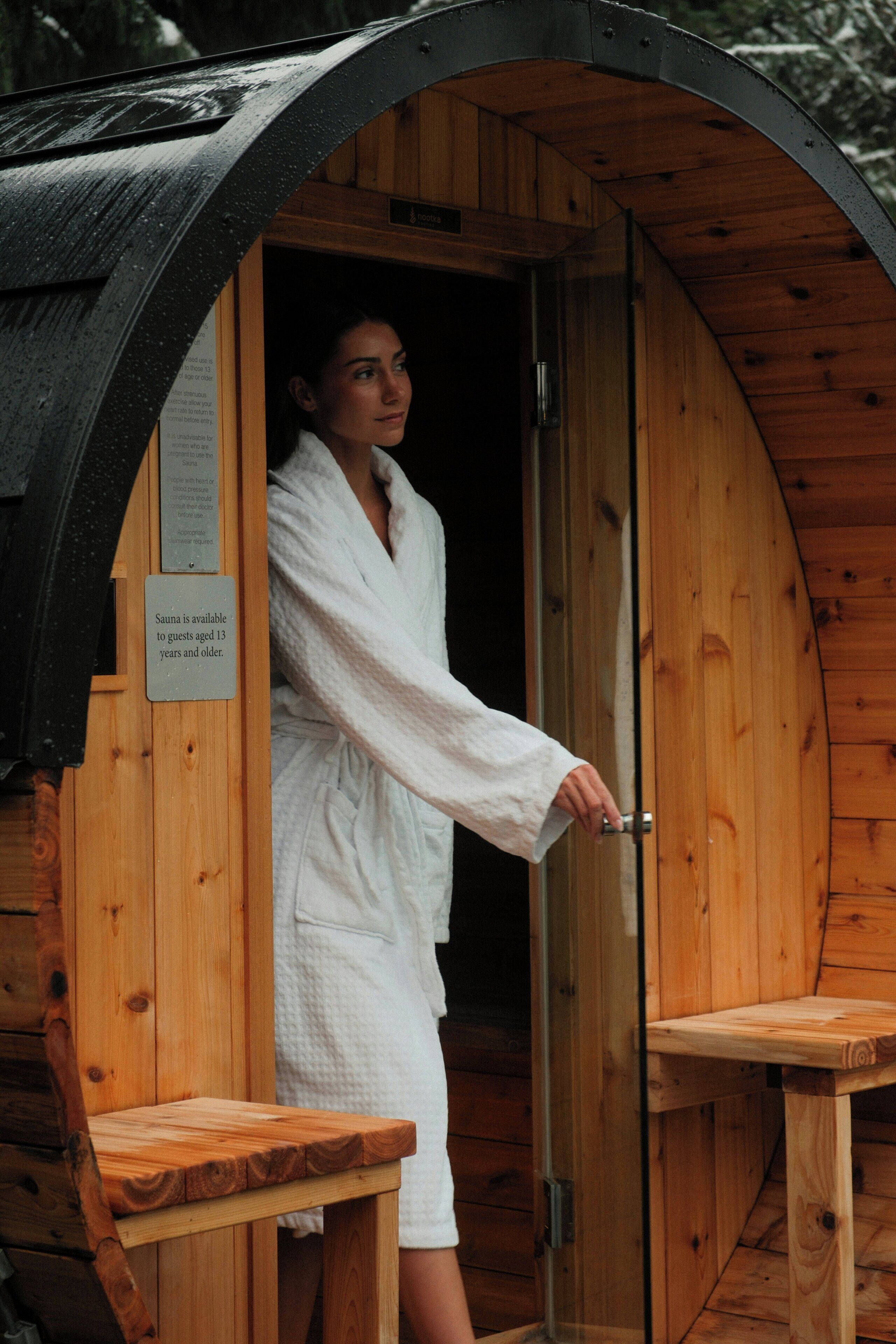 A sauna with a wooden exterior, a glass door, and a sign indicating it is available to guests aged 15 and older.