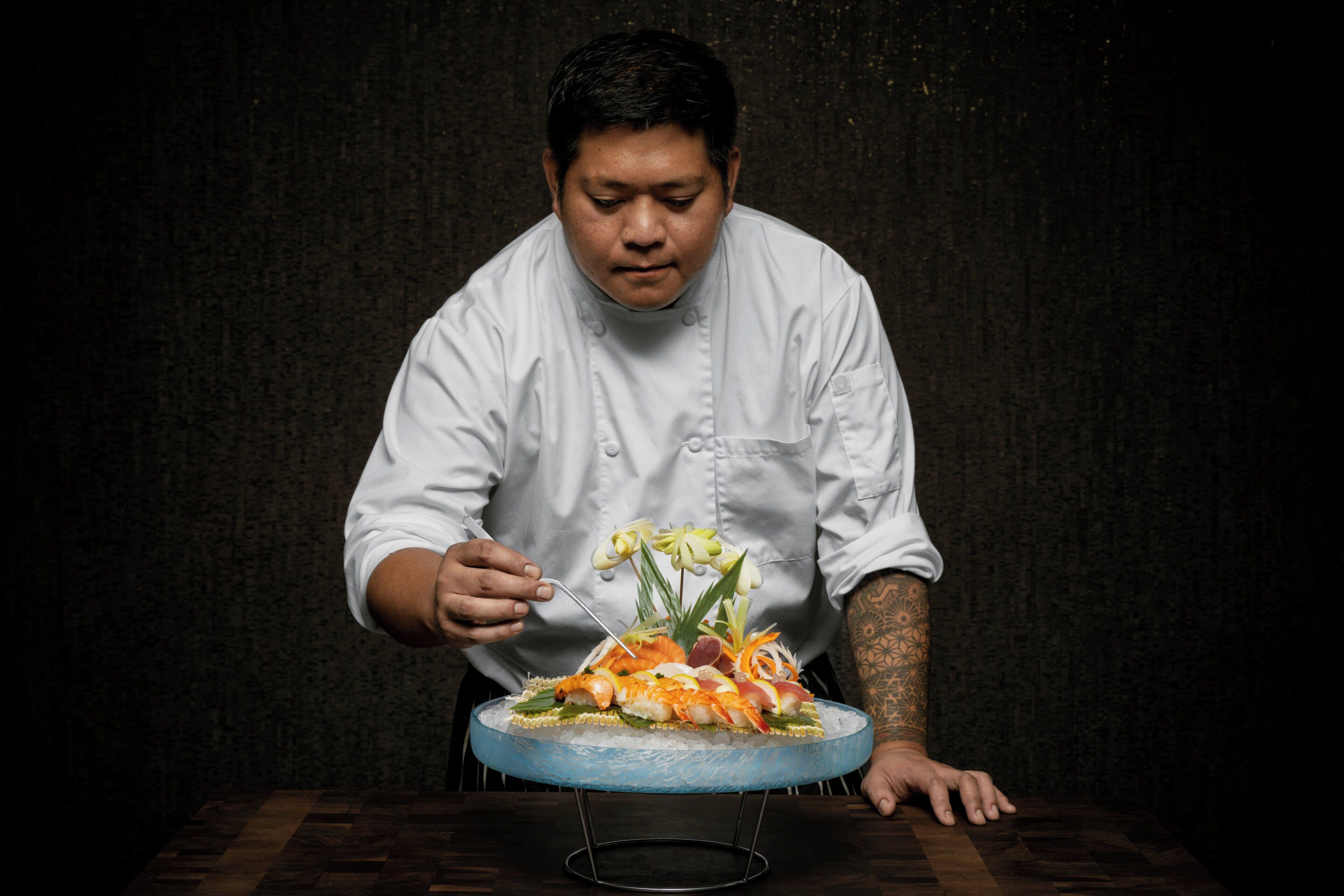 A chef in a white uniform cutting a dish on a blue glass plate.