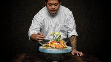 A chef in a white uniform cutting a dish on a blue glass plate.