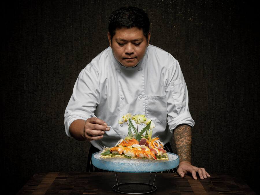A chef in a white uniform cutting a dish on a blue glass plate.