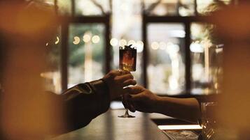 Two hands holding a glass of drink at a bar with a view through large windows.