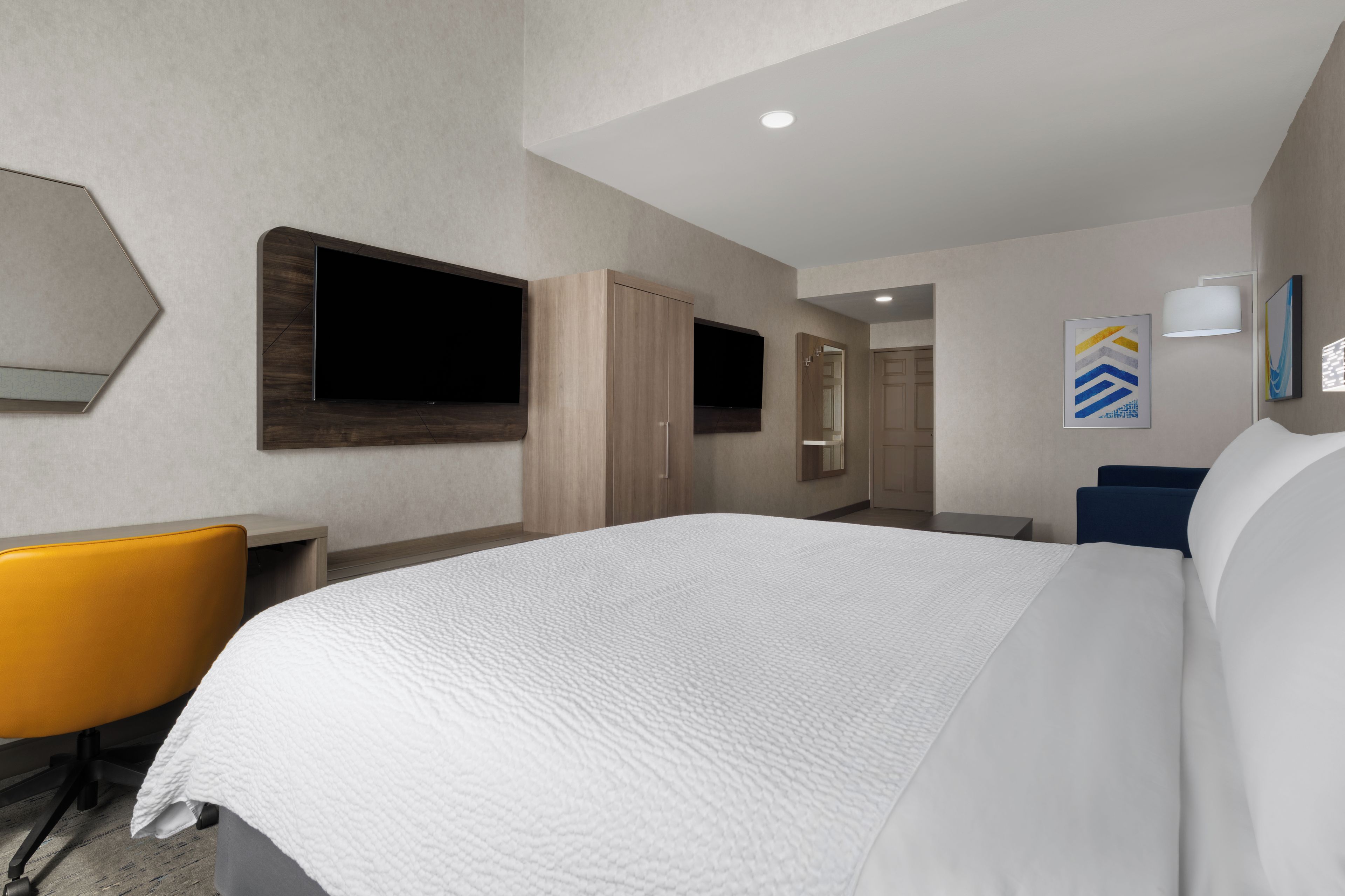 A hotel room with a large bed, a desk with a chair, a flat-screen TV, and a wardrobe.