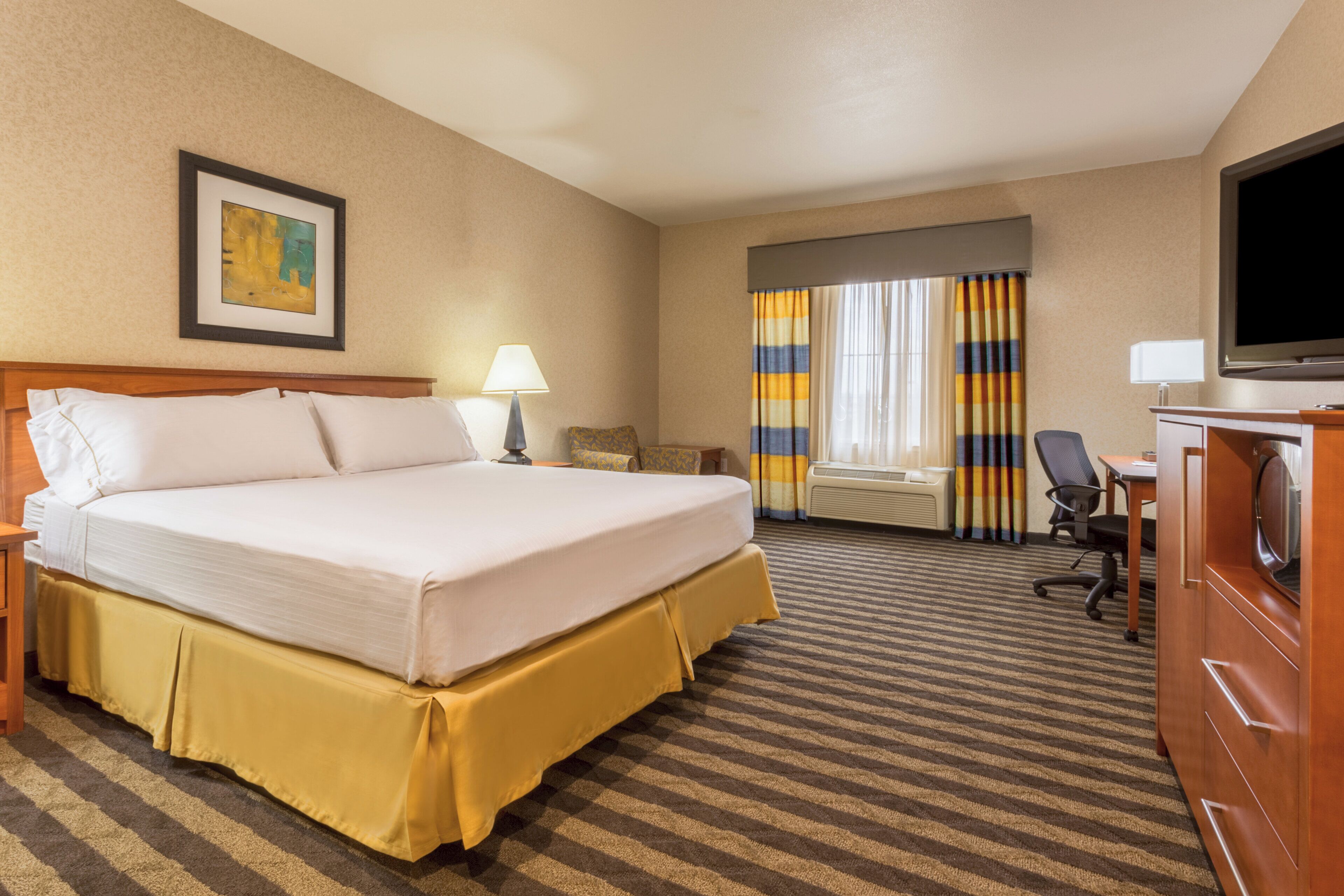 Habitación de hotel con una cama grande, un escritorio con silla, televisión y ventana con cortinas.