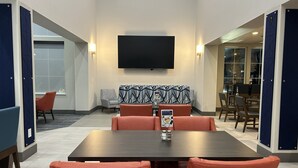 A conference room with a large table, orange chairs, a patterned sofa, and a flat-screen TV on the wall.