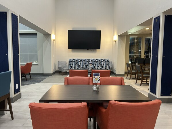 A conference room with a large table, orange chairs, a patterned sofa, and a flat-screen TV on the wall. - Holiday Inn Express Hotel & Suites Manteca by IHG (Manteca)