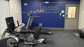 A fitness center with cardio machines, a wall with motivational text, and a door with a phone.