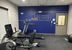 Une salle de sport équipée de machines de cardio, d’un mur orné de messages motivants et d’une porte avec un téléphone.